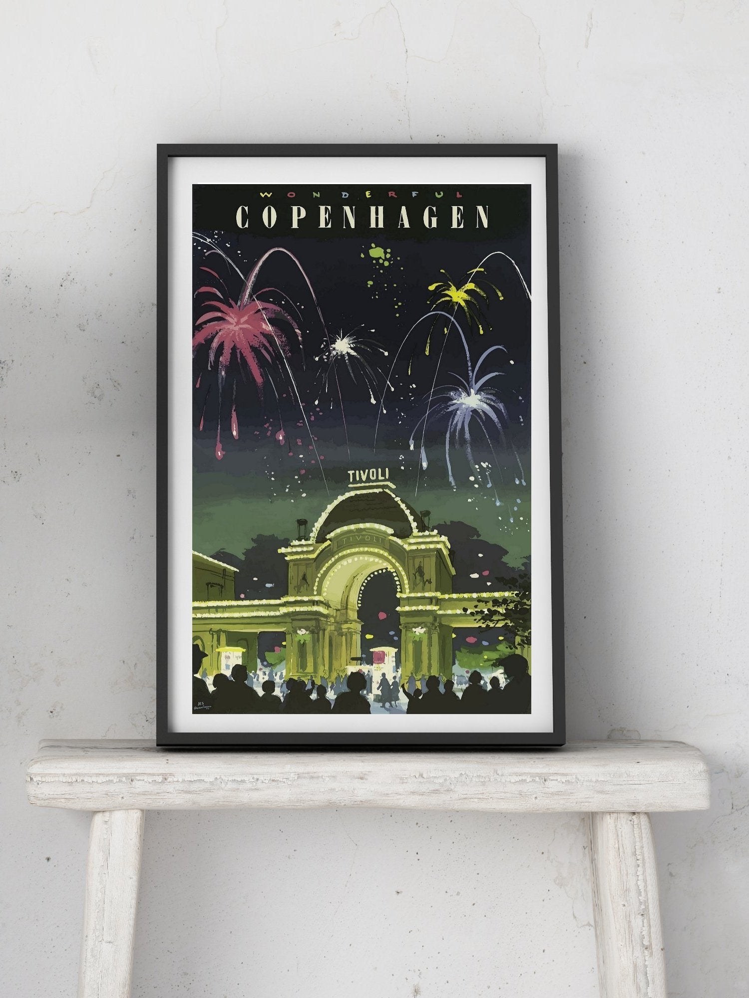 Framed poster of Tivoli Gardens in Copenhagen with fireworks on a white surface and light gray wall background.